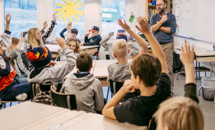 Barn i klassrum som räcker upp handen